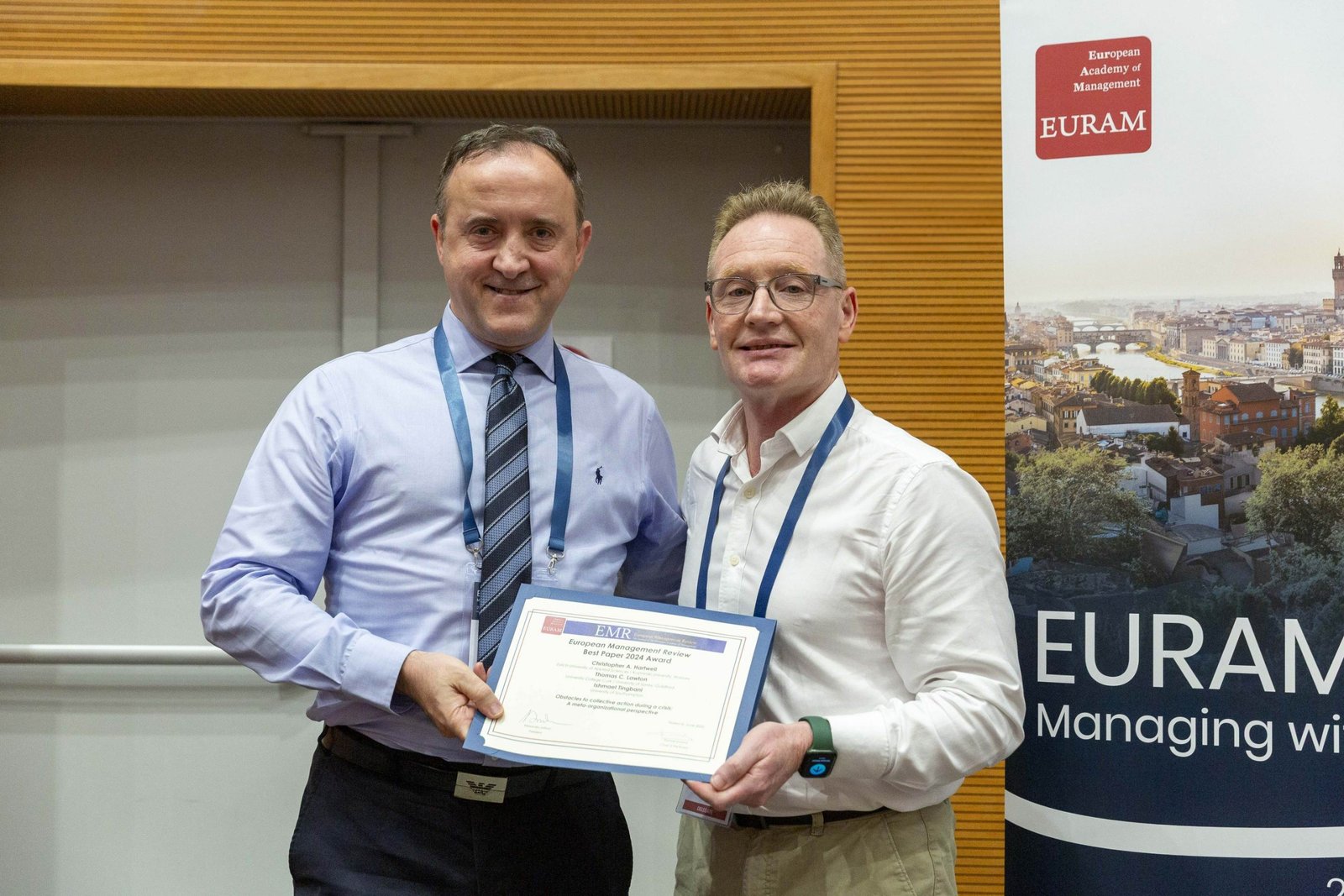 Thomas C. Lawton, right, glasses and white shirt, with a colleague, holding the European Management Review Best Paper 2025 Award in front of a EURAM banner.